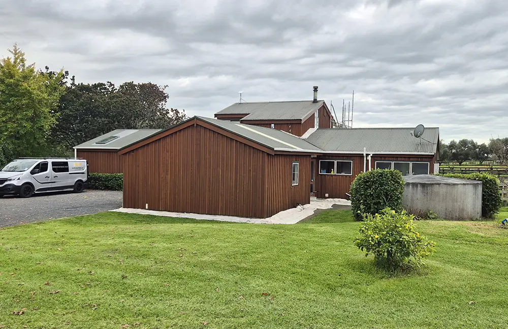 a large house in a rural setting with freshly-painted brown wooden exterior